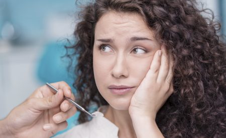 Young beautiful woman suffering from toothache in consulting room